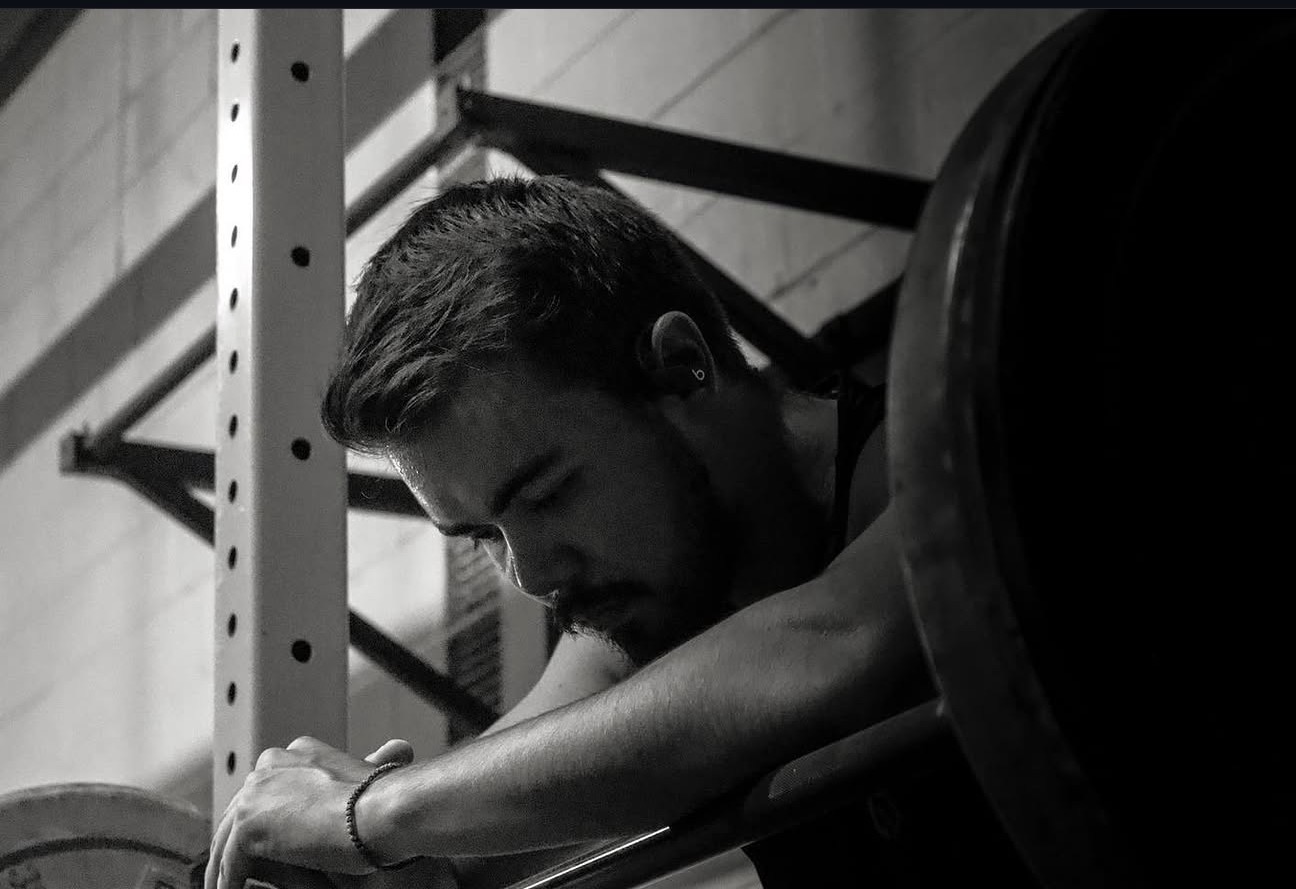 Cameron Sato resting against a loaded barbell between sets